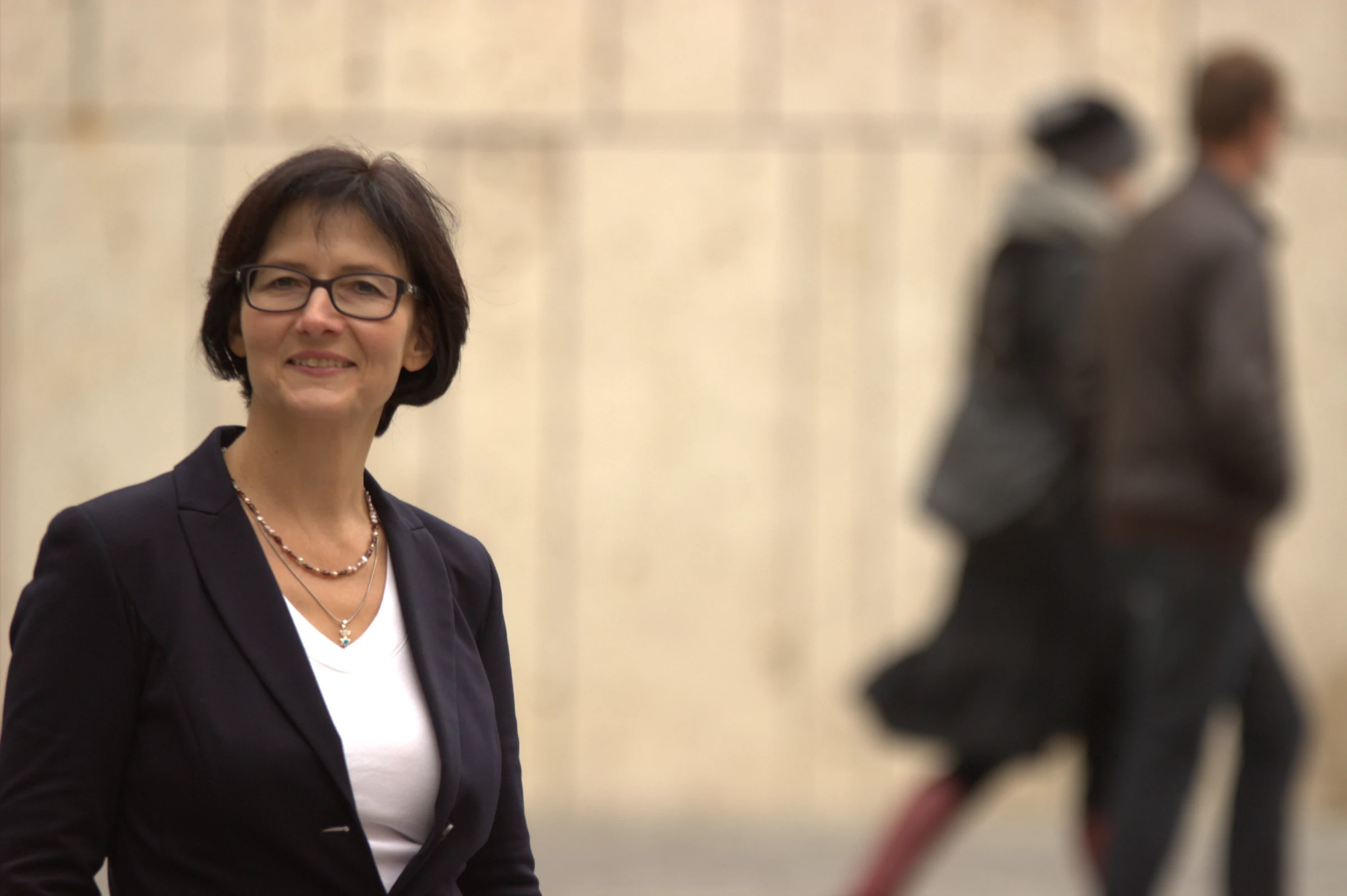 Petra Schmidt vor einer hellen Wand, im Hintergrund ein Paar